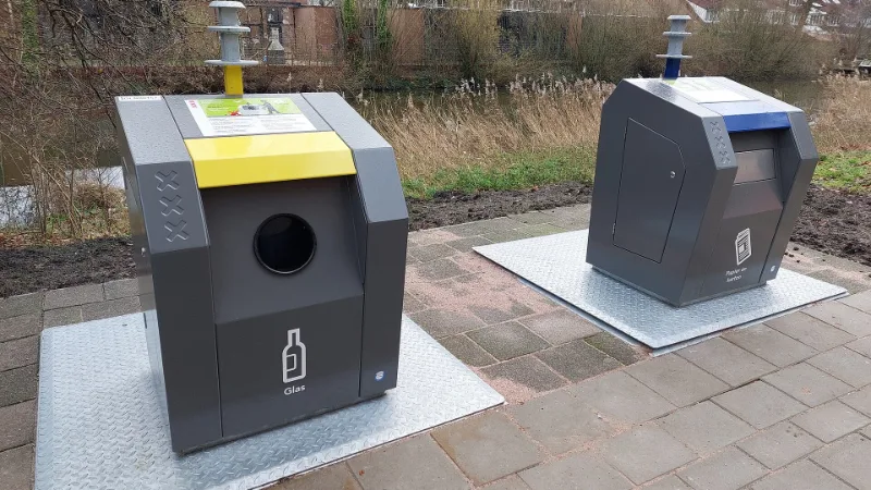 Ondergrondse afvalcontainers in Amsterdam: een gele glasbak en een blauwe papierbak voor gescheiden inzameling.