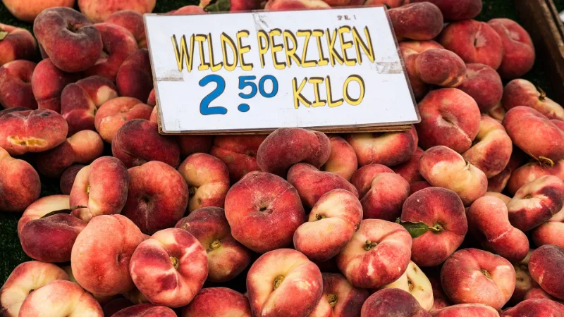 Platte perziken te koop op een fruitkraam op de weekmarkt in Winterswijk, met prijskaartje in euro's.